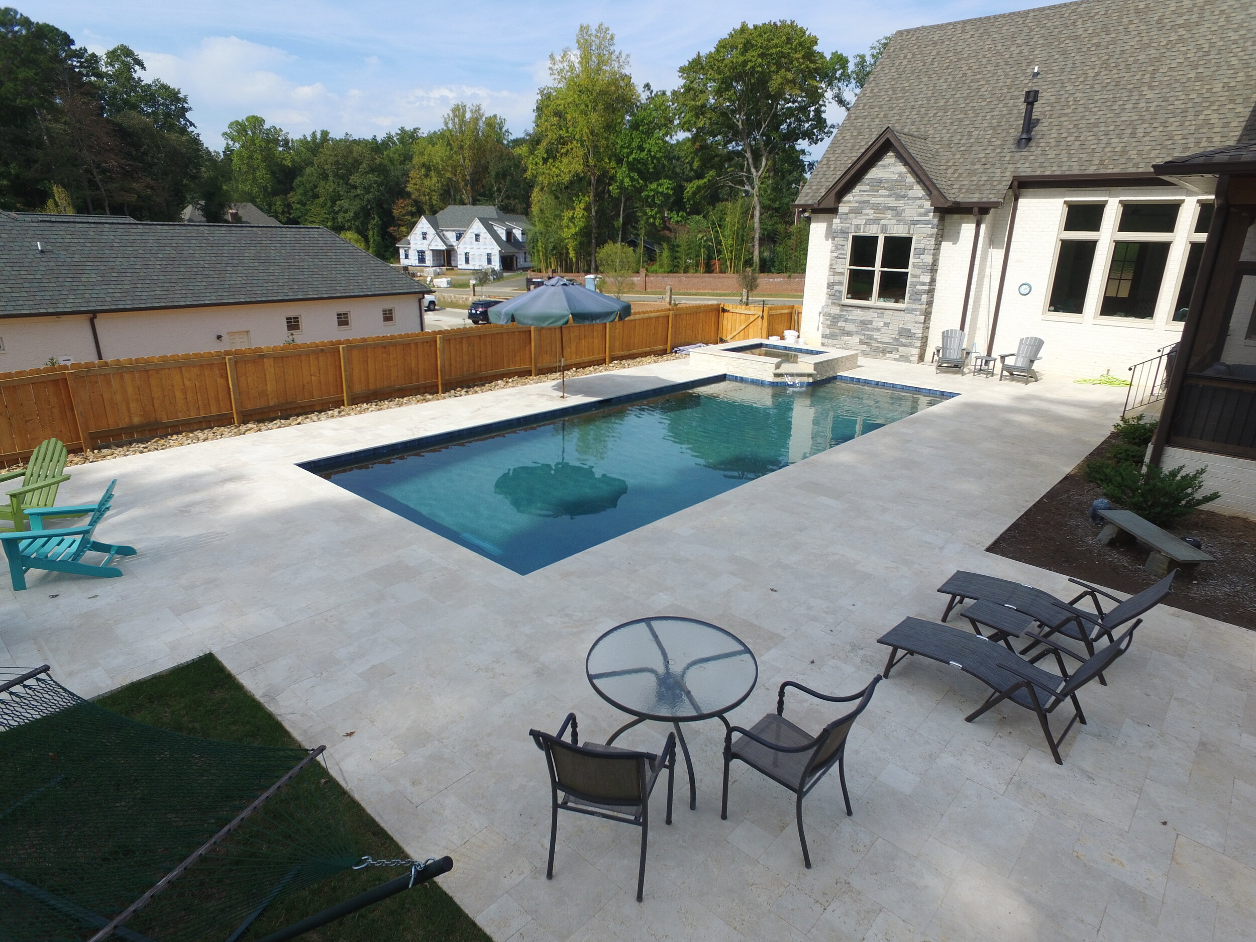 A custom in-ground pool with spillover spa and travertine decking — ADI Pool & Spa, Greensboro NC.